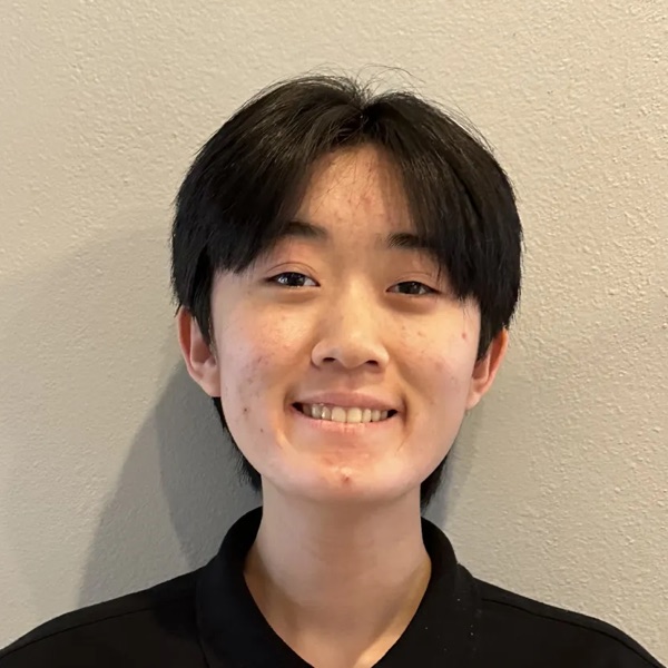 Suzuko Ohshima in a black polo shirt, smiling against a plain cream wall.